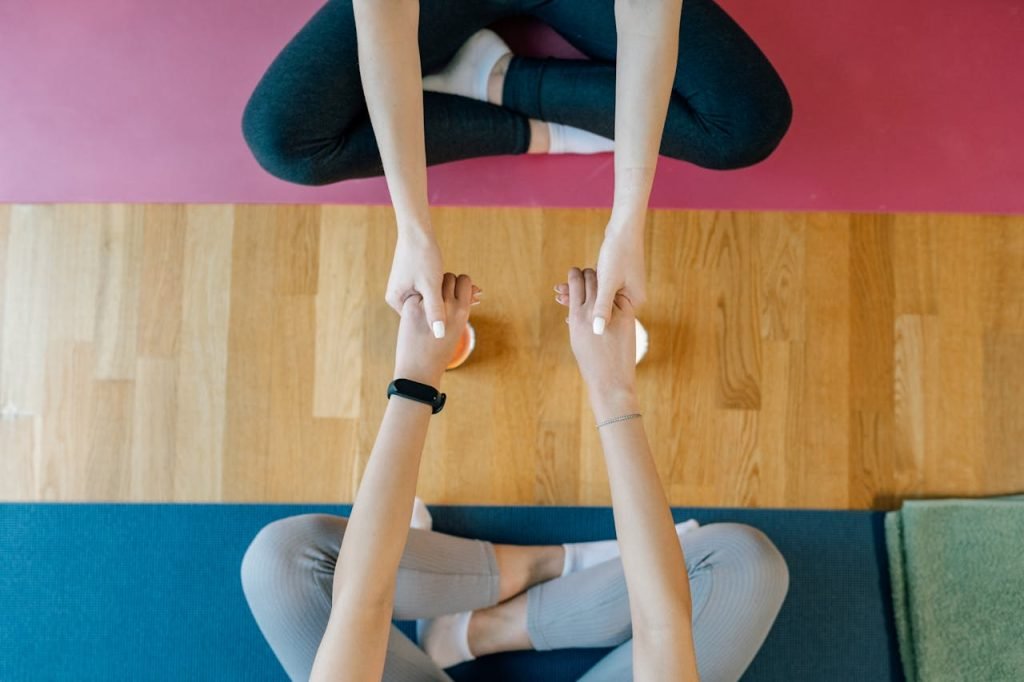 Two people seated on yoga mats holding hands, promoting balance and support.