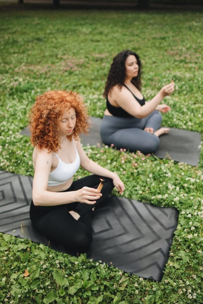 Two women meditating on yoga mats in a park, embracing mindfulness outdoors.